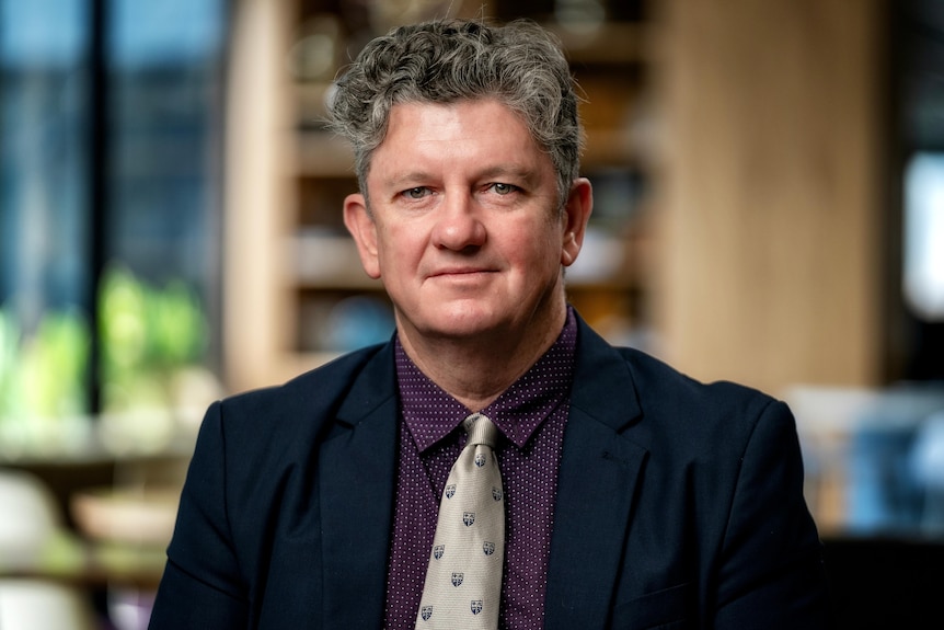 A portrait of Shane Budden wearing a suit and in an office.