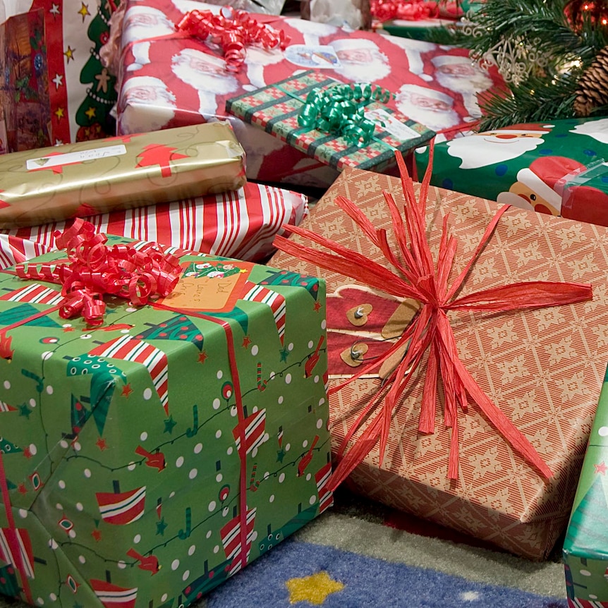 Red and green Christmas presents sit under a tree.