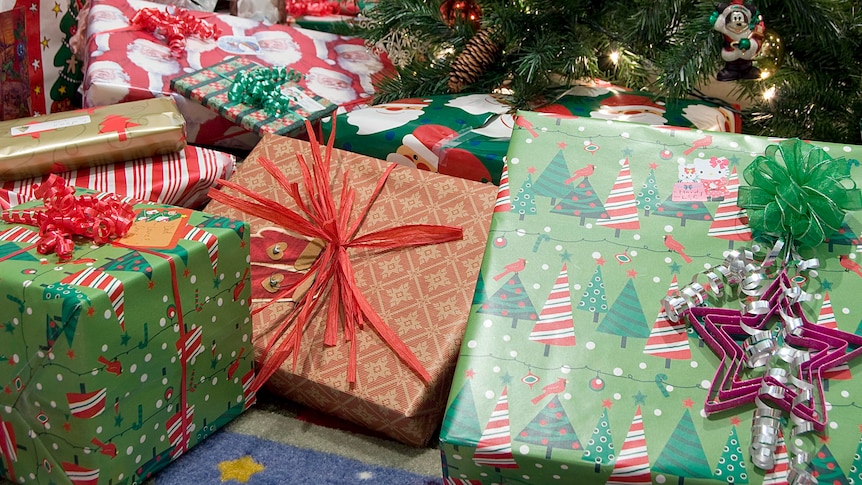 Red and green Christmas presents sit under a tree.