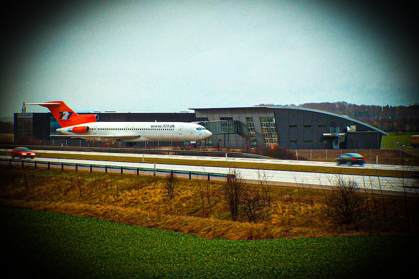 A plane near a highway  beside a building.
