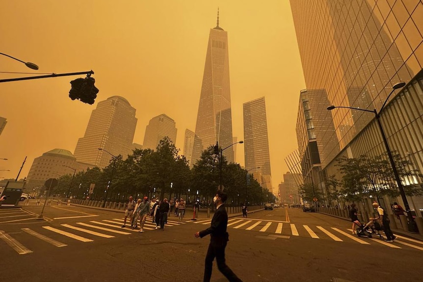 People walking past city skyline amidst orange smokey haze