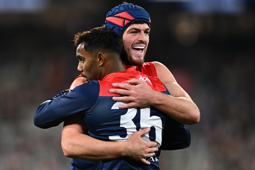 Two Melbourne AFL players embrace as they celebrate a goal against North Melbourne.