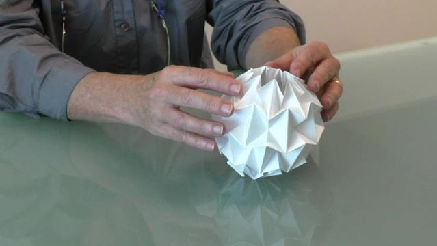 Hands hold paper folded into a complex sphere shape