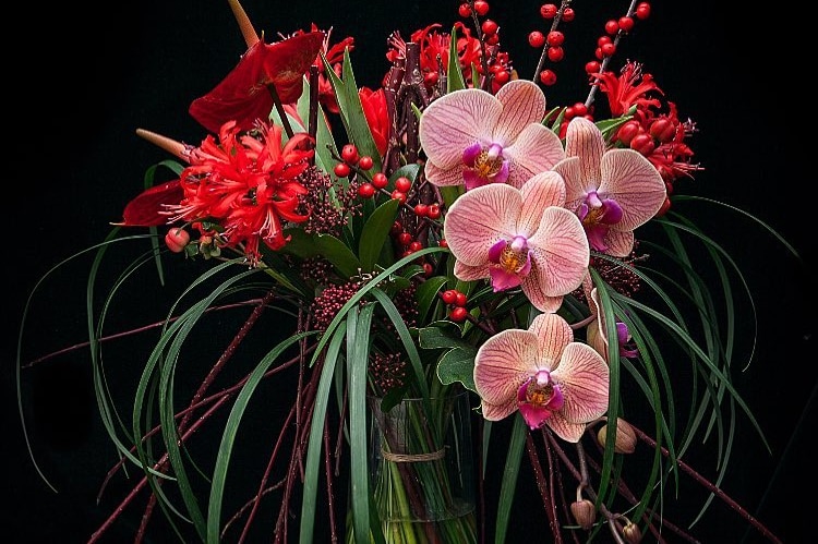 A bouquet of flowers in a glass vase with orchids, vibrant red flowers, seeds and berries.