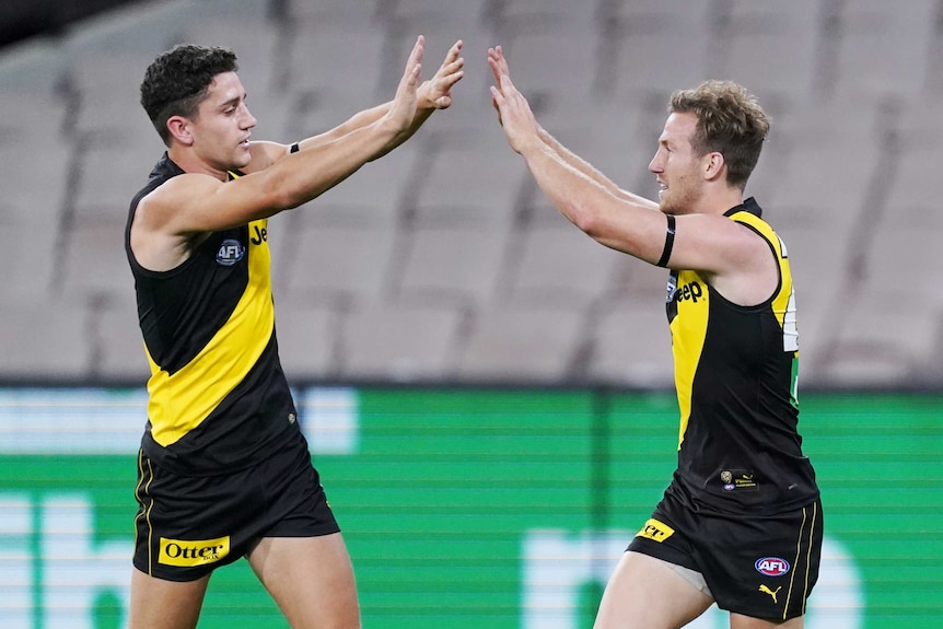 Two Richmond AFL players prepare to give each other a high five as they celebrate a goal at the MCG.