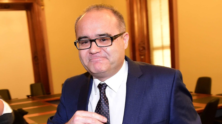 Adam Somyurek wears a navy suit and a spotty tie.