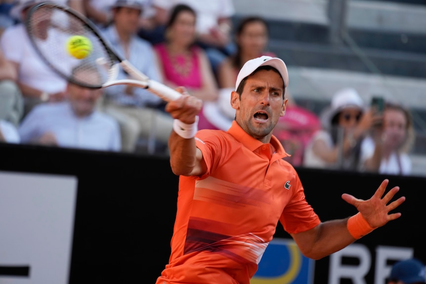 Novak Djokovic has his mouth open as he extends his racquet to hit a forehand return.  