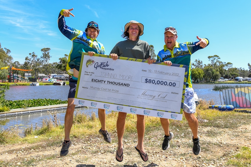 Three men jumping in the air holding an oversized cheque