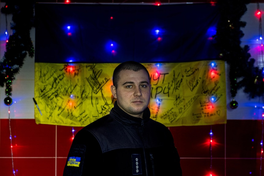 a firefighter with a ukrainian flag path on his arm stands in front of a signed Ukrainian flag and lights