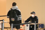 A police officer in a mask speaks to a man in a hoodie and with a backpack