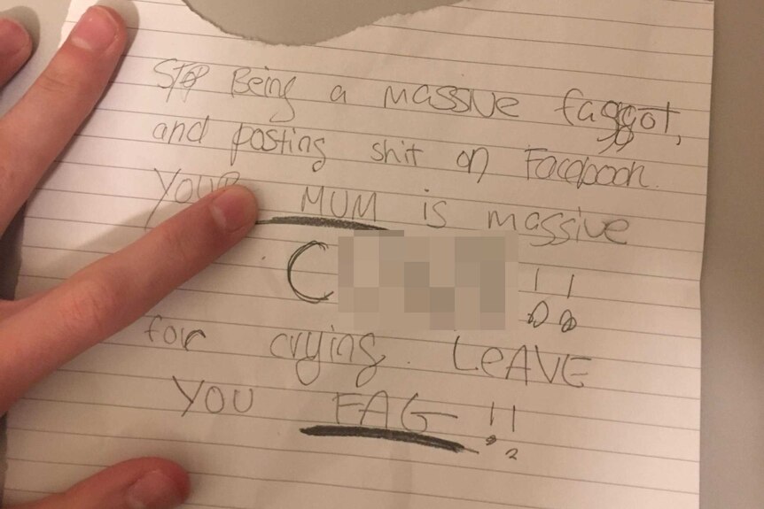 A hand holds a piece of paper with an homophobic message written on it.