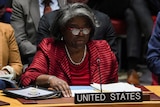 Linda Thomas-Greenfield sits at a desk, flanked by others, with a folder of documents, microphone and a 'United States' sign