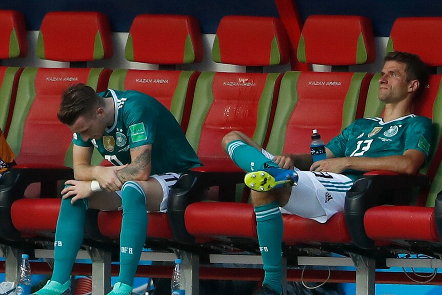 Marco Reus looks down and Thomas Mueller sits on the bench