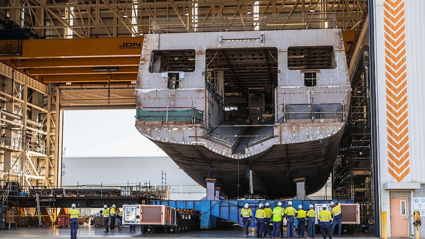 The hull of an huge ship sits inside a warehouse.