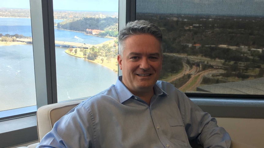 Fed Finance Minister Mathias Cormann sitting in chair in Perth electoral office with Swan River in background, 2016