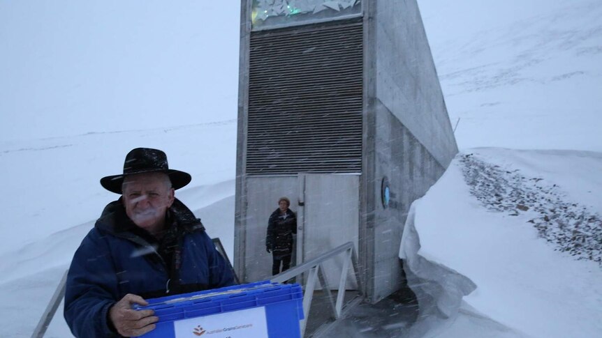 Man in black akubra hat stands in blizzard in front of architecturally significant vault opening in ice mountain, Svalbard