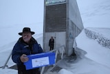 Man in black akubra hat stands in blizzard in front of architecturally significant vault opening in ice mountain, Svalbard