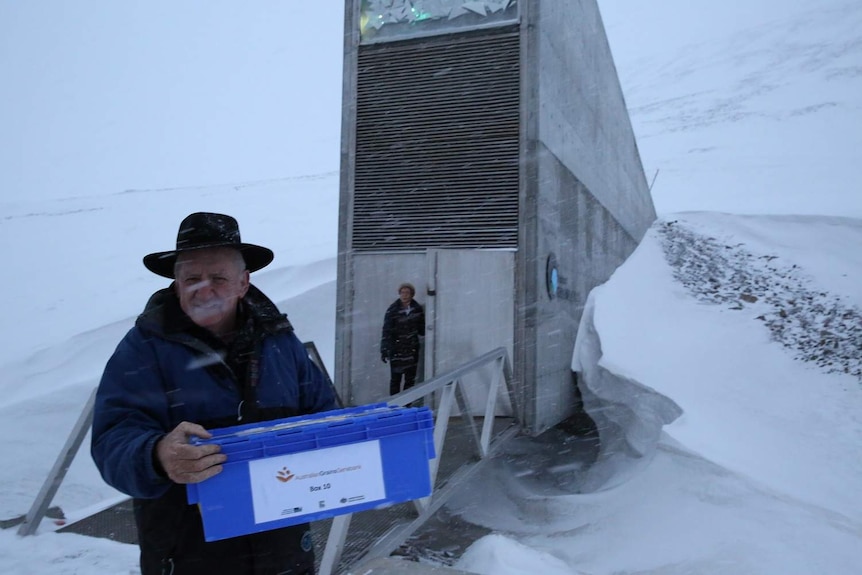 Man in black akubra hat stands in blizzard in front of architecturally significant vault opening in ice mountain, Svalbard