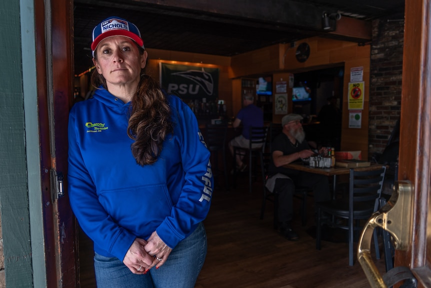 Woman in jeans and blue hoodie leaning against the doorway of a bar.