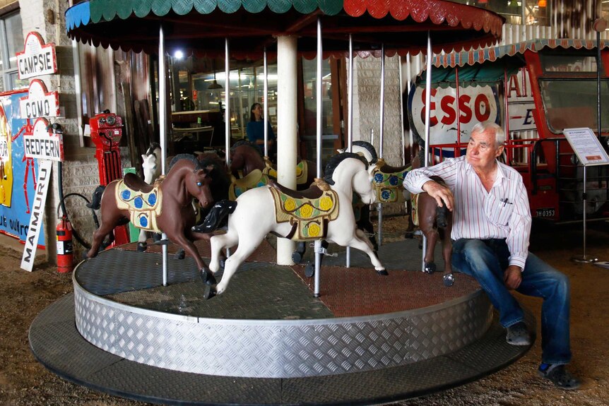 An older man sits on a carousel.