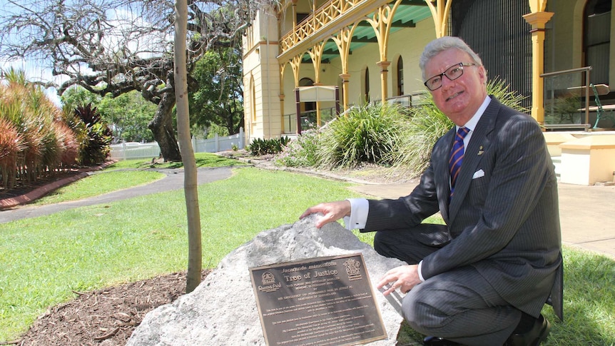 Queensland Governor Paul de Jersey kneels beside the Tree of Justice plaque