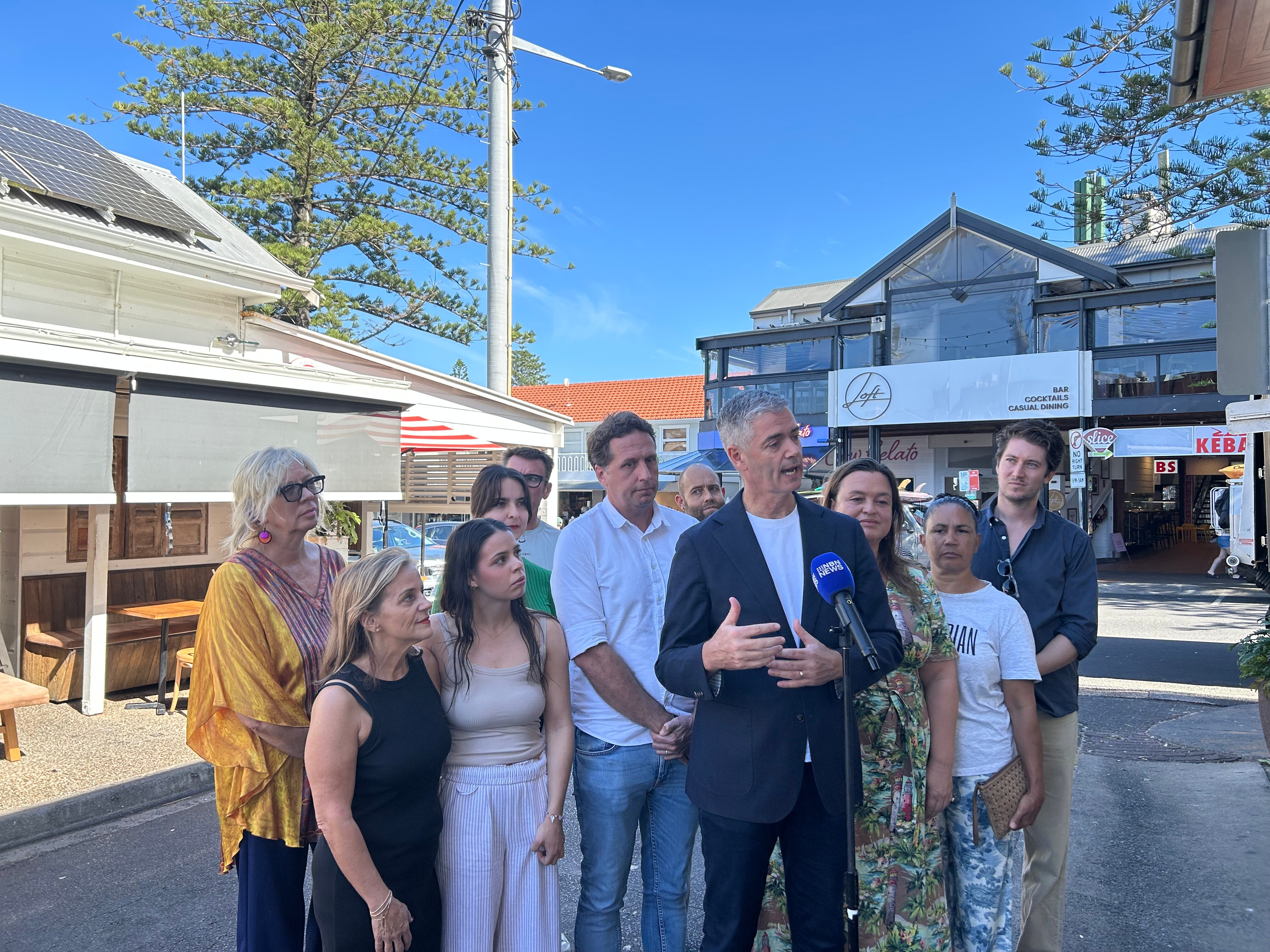 Un hombre frente al micrófono en una calle rodeado de un grupo de personas.