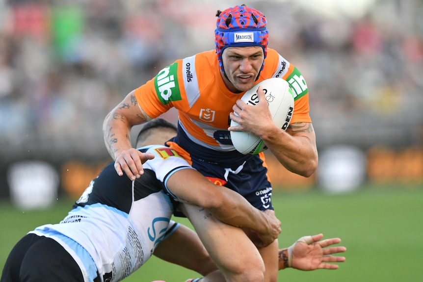 A Newcastle Knights NRL player holds theball with his left hand as he is tackled by a Cronulla opponent.