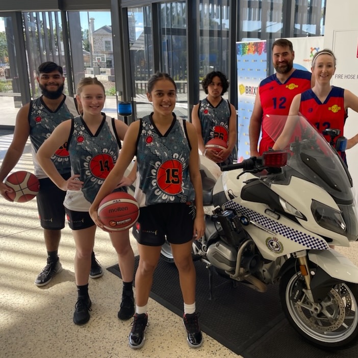 aboriginal boys and girls in basketball uniforms with balls pose near police bike with two adults in red basketball uniforms