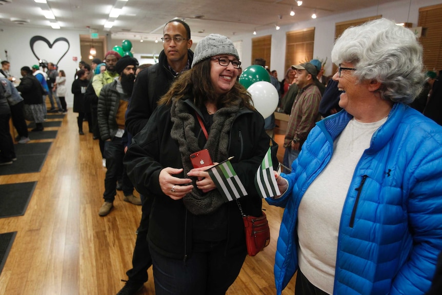 Two women laugh at each other as a long line waits behind them to purchase legal marijuana.