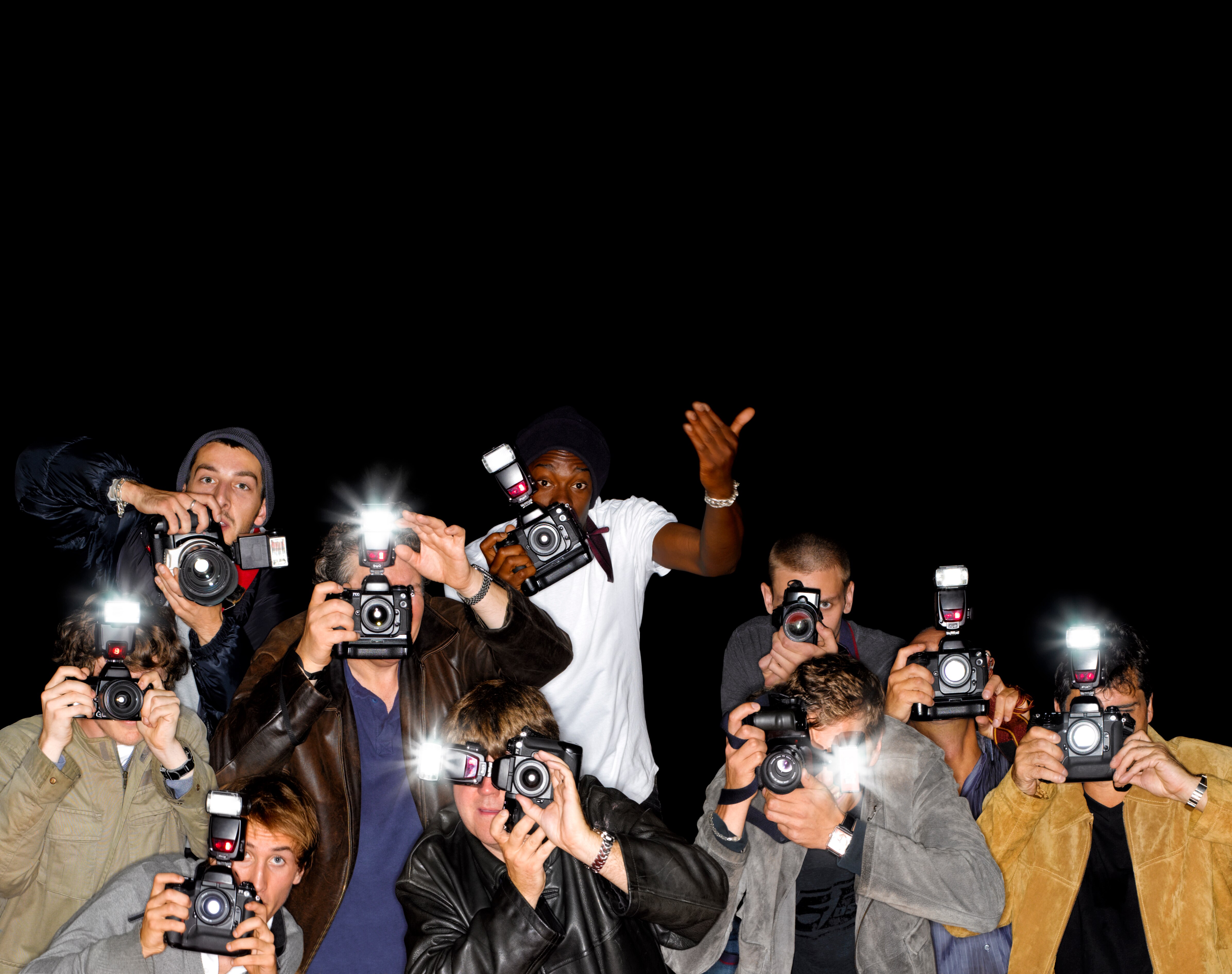 A swarm of paparazzi photographers with flashing cameras.