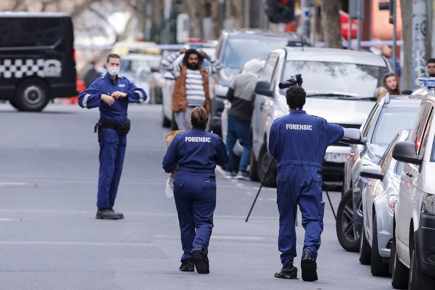 Police forensic officers stand on the street outside the apartment building.