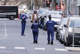 Police forensic officers stand on the street outside the apartment building.