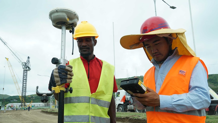 To men wearing hard hats stand on construction site.