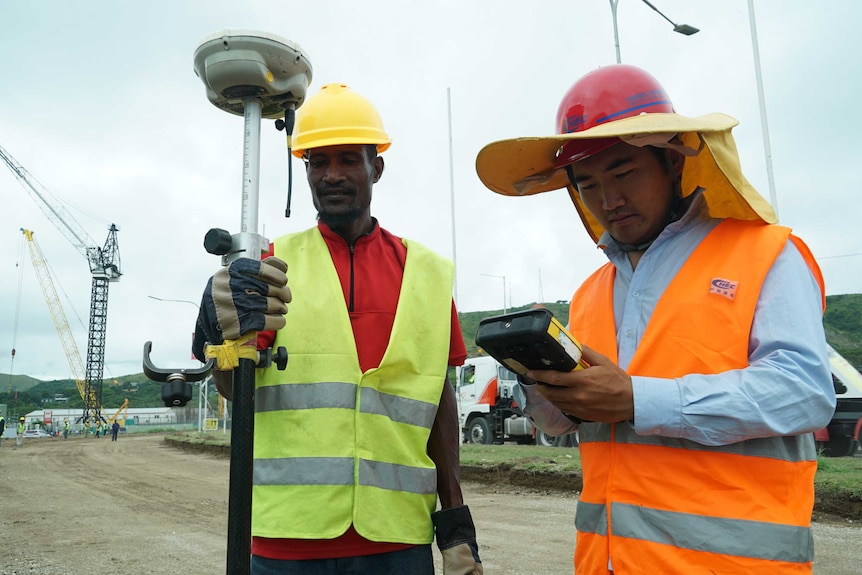 To men wearing hard hats stand on construction site.