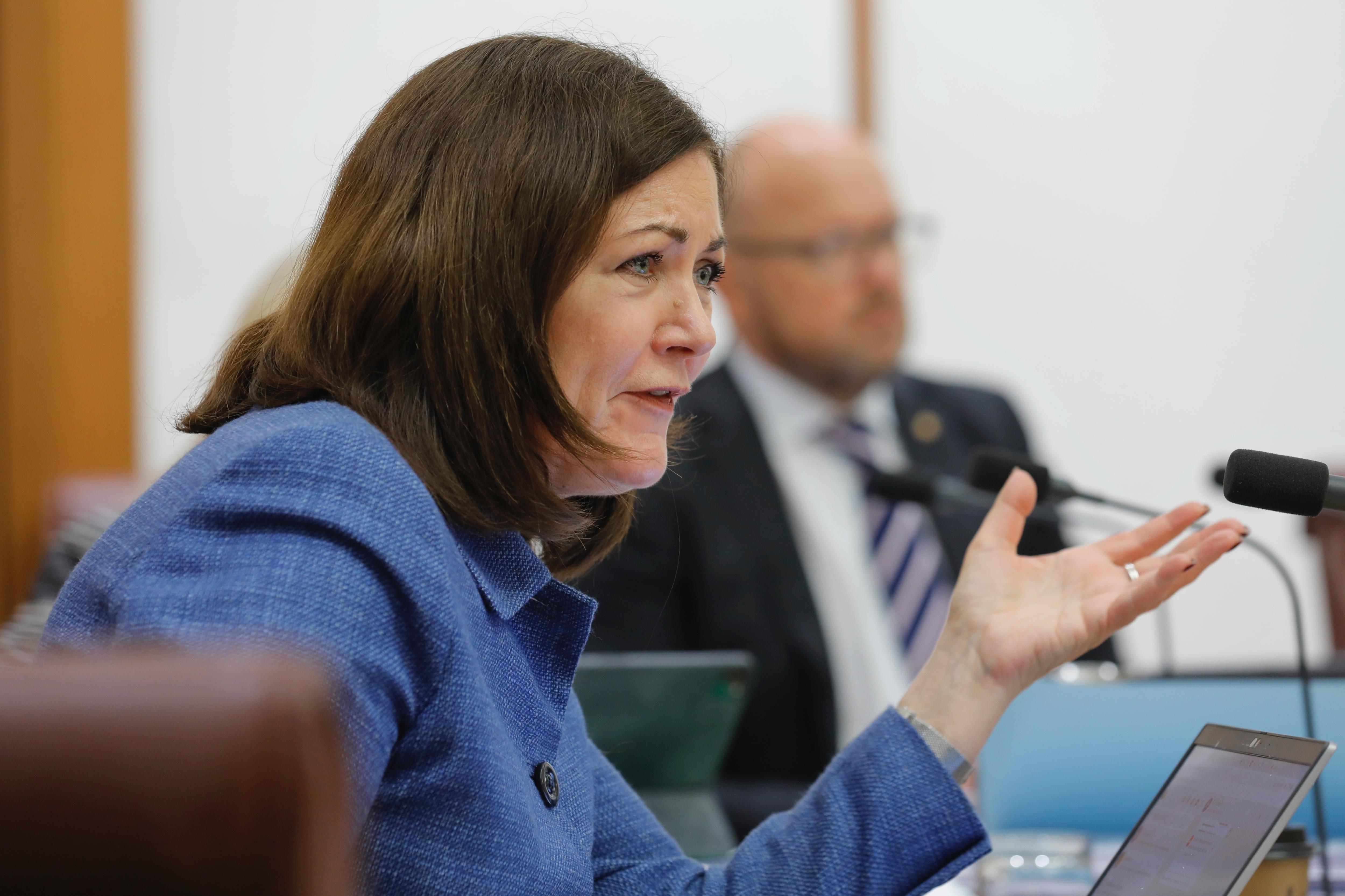 A woman gesticulates and looks quizzical while speaking into a microphone at a senate hearing