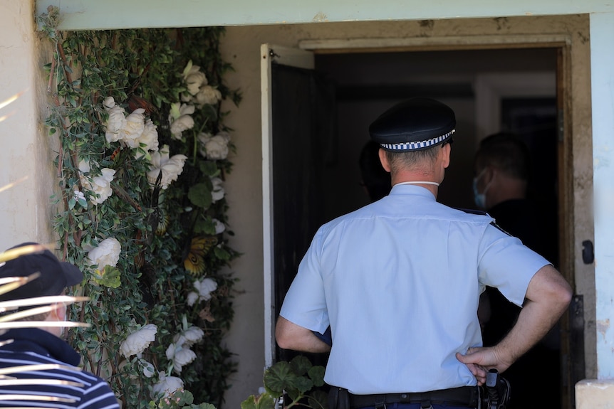 A new south wales police form member stands in the doorway of a house with his back facing the camera
