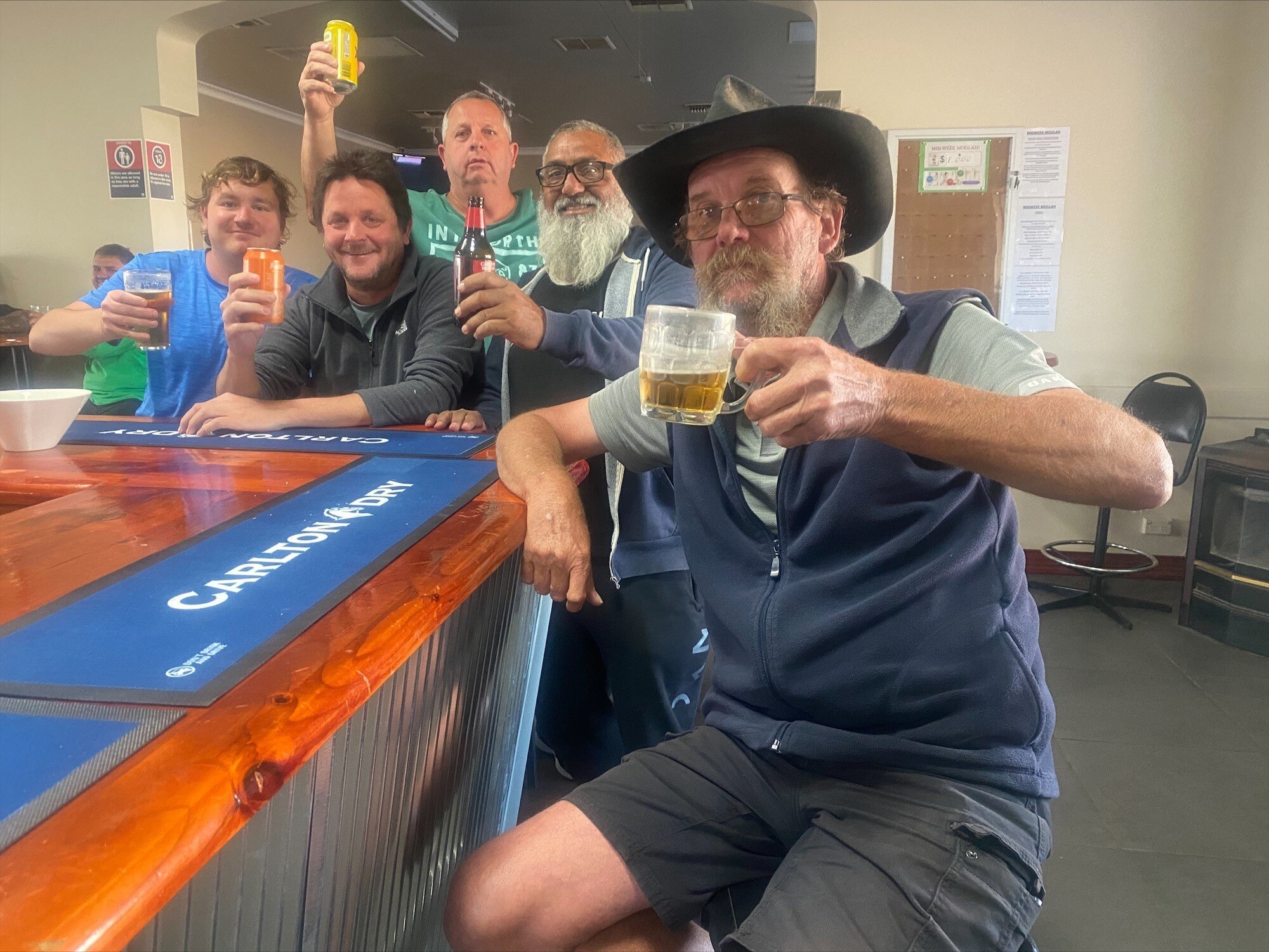 A group of men of varying ages holding drinks and sitting next to a bar in a pub