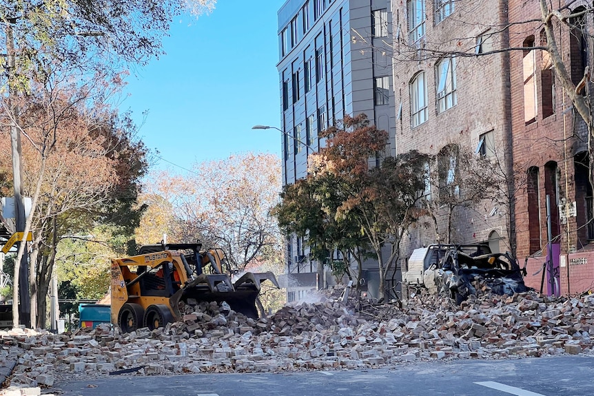 A digger shifts bricks on a street in front of buildings