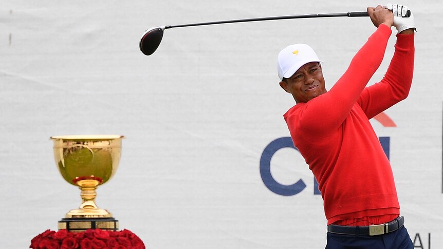 Tiger Woods plays a shot wearing a red jumper in front of the golden President's Cup