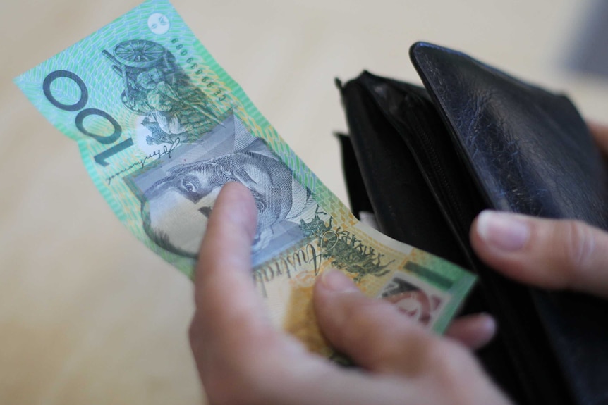 A hand holding a $100 note next to a wallet