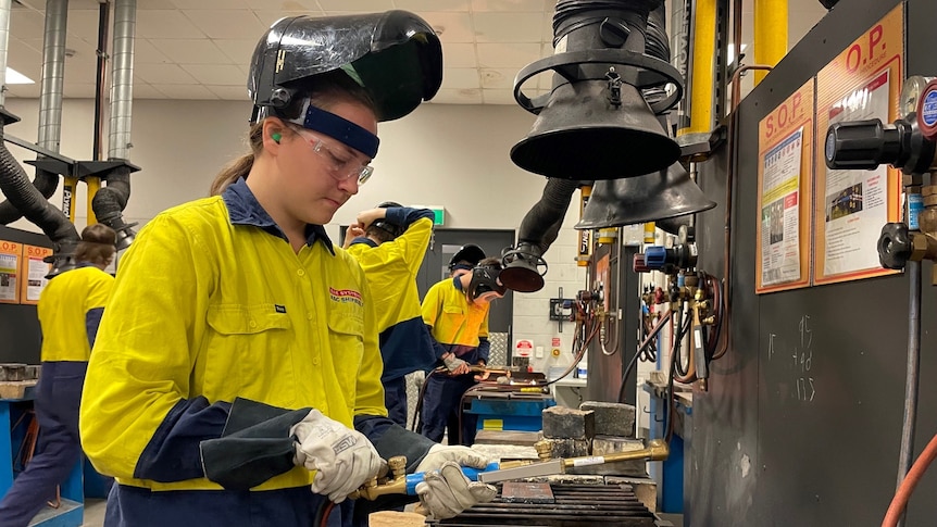 A young woman wearing a welding mask in a workshop