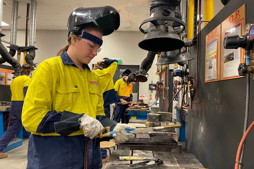 A young woman wearing a welding mask in a workshop