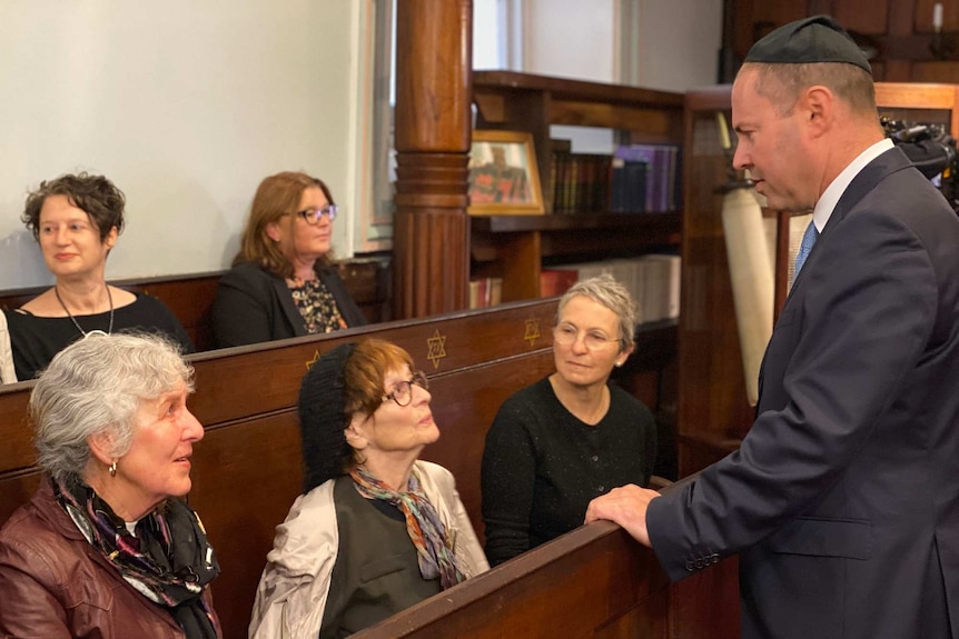 Women sitting inside a synagogue talking to a man.