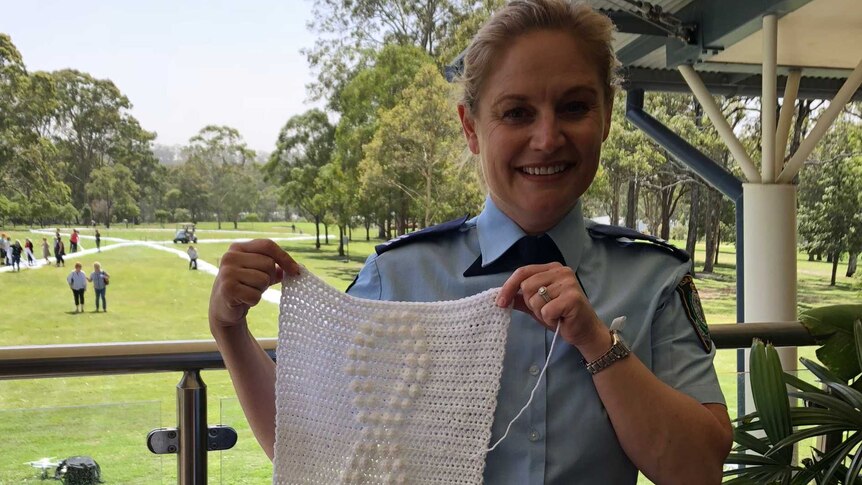 A blonde female police officer holding a long length of white knitting.
