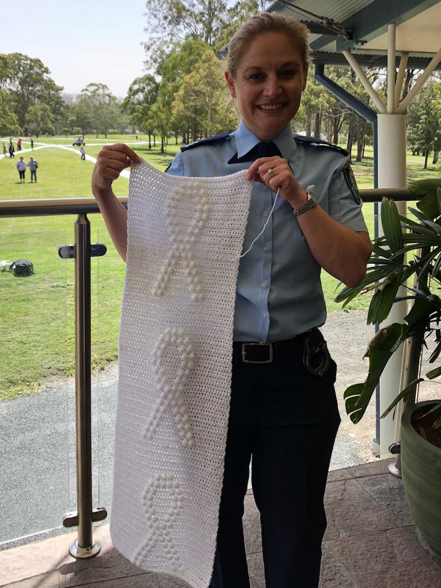 A blonde female police officer holding a long length of white knitting.