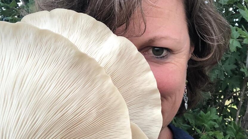 Woman holds a giant mushroom up to her face.