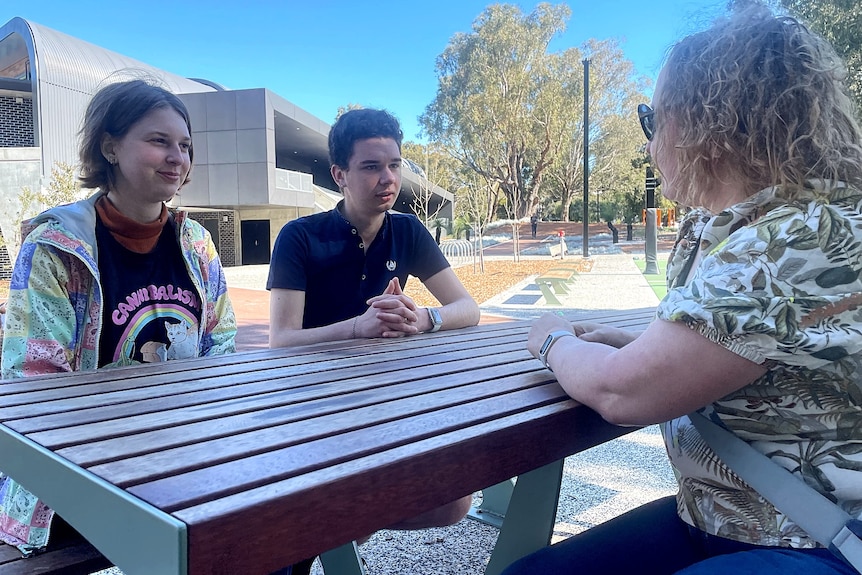 A woman talks to two teenagers at a picnic table