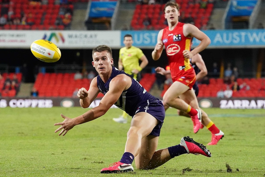 A Fremantle Dockers AFL player handballs to his right against Gold Coast Suns.