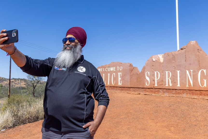 A man in a turban takes a selfie in front of an Alice Springs sign. 