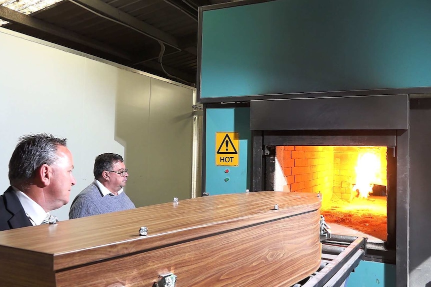 Two men load a coffin into be cremated